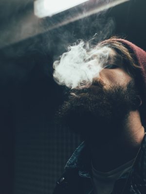 Young male hipster in knit hat smoking at night
